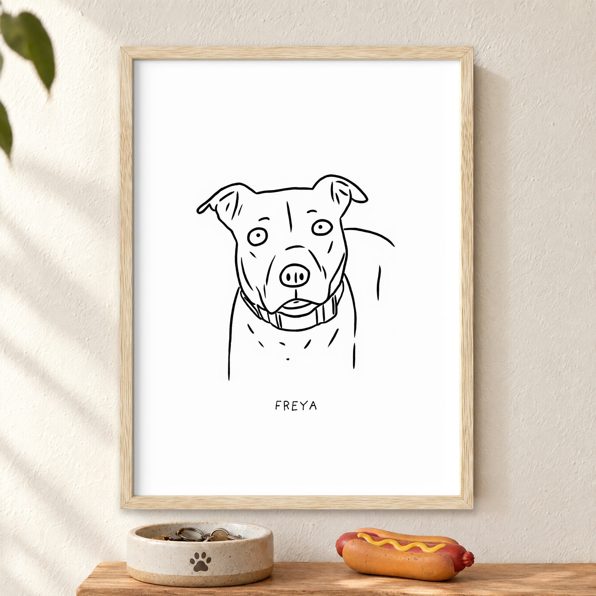 Freya portrait in a natural wood frame above a shelf with a bowl and toy hot dog